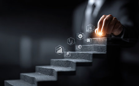 A person in a suit is shown interacting with holographic icons above a staircase. The image features a dark, blurred background and a focus on the hand. The composition uses a shallow depth of field, with soft lighting and a conceptual feel, making it suitable for business and technology themes.の素材