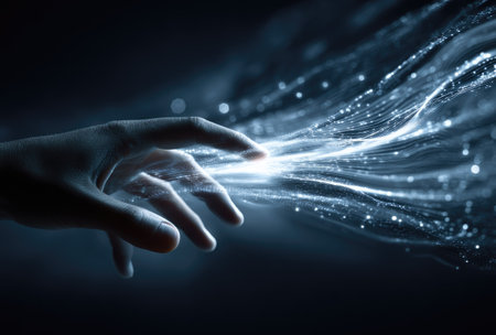 A human hand extends towards a radiant stream of glowing light, featuring particles against a dark background. The image exhibits a cool color palette with high contrast, suggesting a digital or conceptual art style. It may be suitable for illustrating themes of technology, innovation, or connectivity for various commercial or editorial uses.の素材