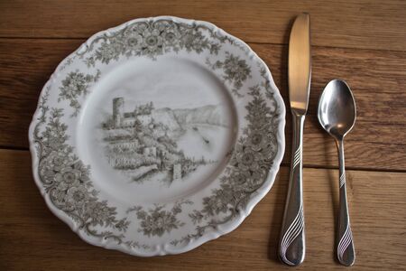 Hand-painted porcelain plate with cutlery on a massive wooden table backgroundの写真素材