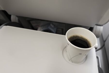Coffee mug with black coffee in the plane on a folding table. Eating and drinking on the plane.の写真素材