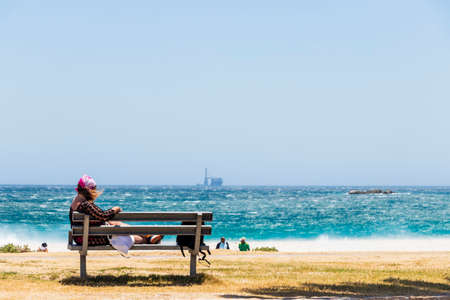 Woman on a bench on the extremely windy beach in Camps Bay, Cape Town.の写真素材