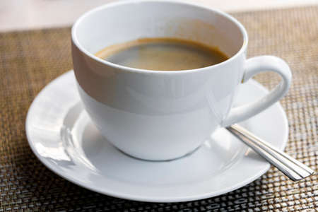 Black coffee crema in a white cup with spoon on a table in Luang Prabang Laos.