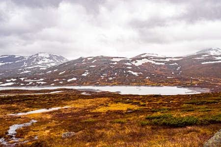 Amazing Vavatn lake panorama rough landscape view rocks boulders and mountains with snow during...
