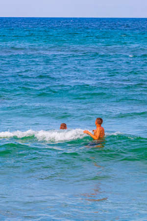 People swim in the turquoise water of the rough natural coastal and beach landscape panorama in Can...