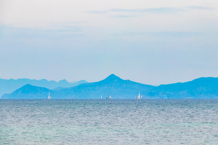 Natural green turquoise beach and water with sailing boats and mountains in Vouliagmeni Beach near to Voula in Greece.の写真素材