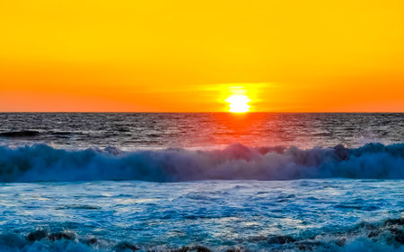 Beautiful stunning colorful and golden sunset in yellow orange red on beach and big wave panorama in tropical nature in Zicatela Puerto Escondido Oaxaca Mexico.の写真素材