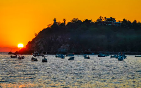 Beautiful stunning colorful and golden sunset in yellow orange red on beach fisher boats and waves panorama in tropical nature in Zicatela Puerto Escondido Oaxaca Mexico.の写真素材