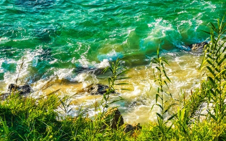 Beach sand turquoise blue water rocks cliffs boulders sun loungers people palm trees and huge big surfer waves on the beach Playa Carrizalillo in Puerto Escondido Oaxaca Mexico.の写真素材