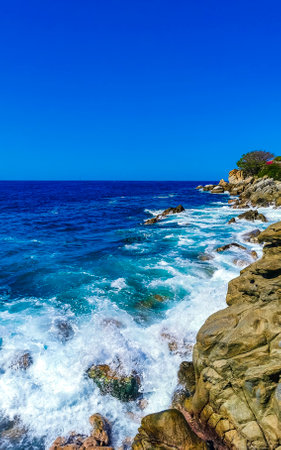 Blue turquoise water and extremely beautiful huge big surfer waves rocks cliffs stones mountains and boulders on the beach in Zicatela Puerto Escondido Oaxaca Mexico.の写真素材