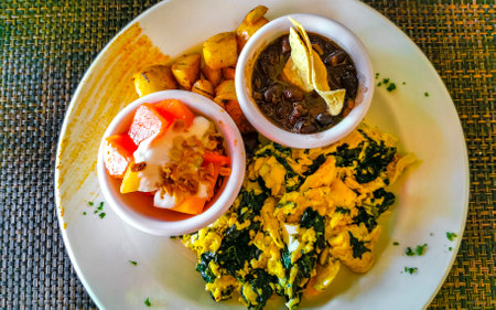 Mexican breakfast with scrambled eggs with spinach fruit and potatoes nicely arranged on white plate...