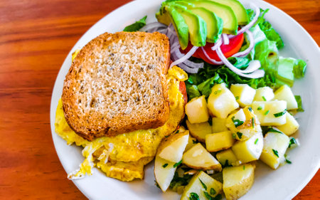 Toast with scrambled eggs salad with onions avocado tomatoes and potatoes on white plate in Zicatela...