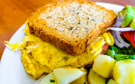 Toast with scrambled eggs salad with onions avocado tomatoes and potatoes on white plate in Zicatela...