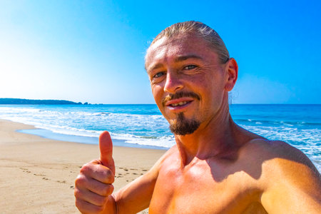 Male tourist traveler man makes selfie with beautiful rocks cliffs stones boulders and huge big surfer waves and natural panorama view on the beach in Puerto Escondido Oaxaca Mexico.の写真素材