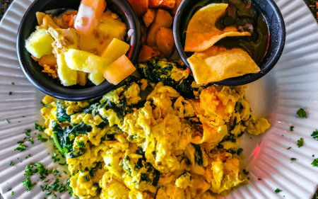 Mexican breakfast with scrambled eggs with spinach fruit and potatoes nicely arranged on white plate...