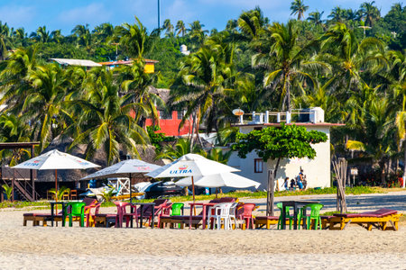 Puerto Escondido Oaxaca Mexico November 13, 2022 Parasols umbrellas sun loungers palms people rocks and waves at the tropical Mexican beach in Zicatela Puerto Escondido Oaxaca Mexico.のeditorial素材