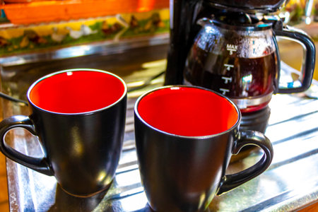 Red and black cup cups of black Americano coffee and coffee maker hot and stylish on a wooden table.の写真素材
