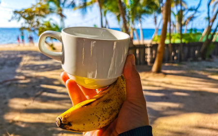 Cup of coffee and a banana in the hand at Caribbean beach in Cancun Quintana Roo Mexico.の写真素材