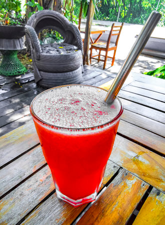 A glass of watermelon juice on a wooden table with tire furniture in the backgroundの写真素材