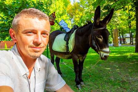 Man handsome tourist with donkey with saddle in the green park in Leninskiy Rayon Brest Brest District Brest Region Belarus.の写真素材