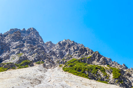 Dangerous falling rocks and stone avalanche from the mountain hill peak in summer with blue sky in the Alps Imst Tyrol Austria.の写真素材