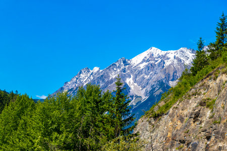 Mountain and alpine hill landscape mountains rocks and peaks panorama of Lechtal alps with green field meadow village forest huts snow and blue sky in Fliess Landeck Tyrol Austria.の写真素材