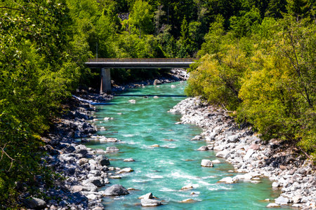 Turquoise blue and green river steam and waterfall Inn with bridge stones rocks grass trees nature and mountain panorama in the Alps FlieÃ Landeck Tyrol Austria.の写真素材