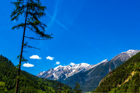 Mountain and alpine hill landscape mountains rocks and peaks panorama of Lechtal alps with green fields meadows snow and blue sky behind forest tree trees in Fliess Landeck Tyrol Austria.の写真素材