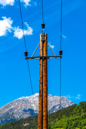 Power pole electricity pylon at mountain and alpine hill landscape mountains rocks and peaks panorama of Lechtal alps with snow nature and blue sky in the Alps Fliess Landeck Tyrol Austria.の写真素材