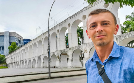 Handsome man male tourist and traveler Arcos da Lapa bridge and City Streets Panorama with arches blue cloudy sky Cars and People in Rio de Janeiro Brazil.の写真素材