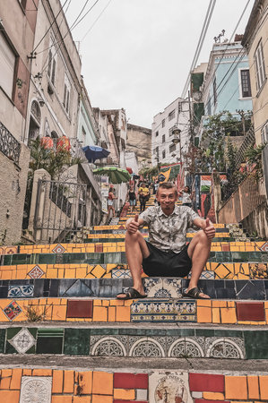 Handsome man male tourist and traveler on Escadaria Selaron the red famous stairs stair step steps...