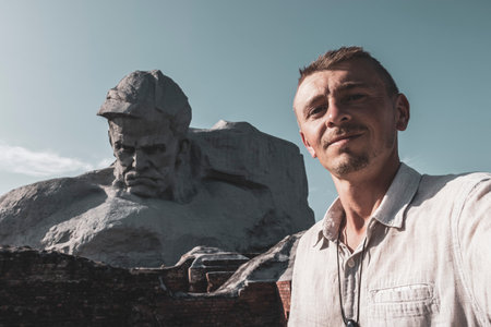 Handsome man male tourist with Monumet Muzhestvo massive gray stone rock sculpture statue at the Brest Fortress in Leninskiy Rayon Brest Brest District Brest Region Belarus.の写真素材