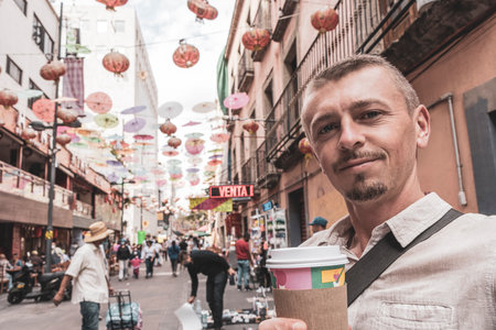 Handsome Man Tourist with Coffee in China Town Chinatown Tourist Street People Chinese Lantern Colorful Parasols and Shops in Centro Historico Mexico City Mexico.の写真素材
