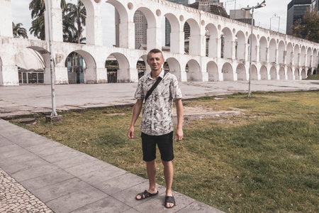Handsome man male tourist and traveler Arcos da Lapa bridge and City Streets Panorama with arches blue cloudy sky Cars and People in Rio de Janeiro Brazil.の写真素材