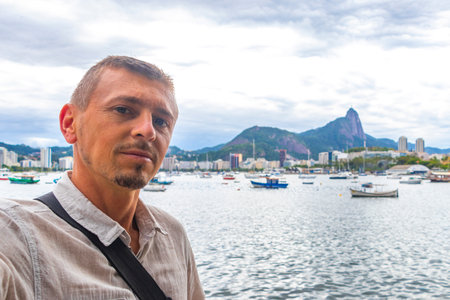 Handsome man tourist takes selfie in the Urca Village coastal and beach promenade with street sidewalk pier harbor jetty yachts and boats in Rio de Janeiro Brazil.の写真素材