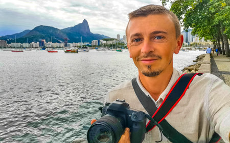 Handsome man tourist takes selfie in the Urca Village coastal and beach promenade with street sidewalk pier harbor jetty yachts and boats in Rio de Janeiro Brazil.の写真素材