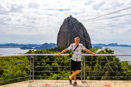 Handsome Tourist Traveler Man is Posing at the Sugarloaf Sugar Loaf Mountain Hill Rock Pao de Acucar Panorama View in the Urca Village of Rio de Janeiro Brazil.の写真素材
