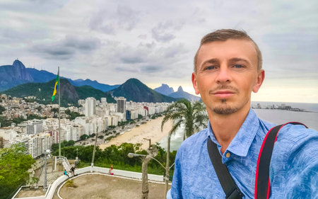 Handsome Man Tourist with the Rio de Janeiro Panorama View of the City Skyline Beaches Beach Coast Sea Mountains Tropical Forest and Blue Cloudy Sky in State of Rio de Janeiro Brazil.の写真素材