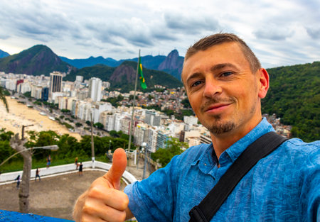 Handsome Man Tourist with the Rio de Janeiro Panorama View of the City Skyline Beaches Beach Coast Sea Mountains Tropical Forest and Blue Cloudy Sky in State of Rio de Janeiro Brazil.の写真素材