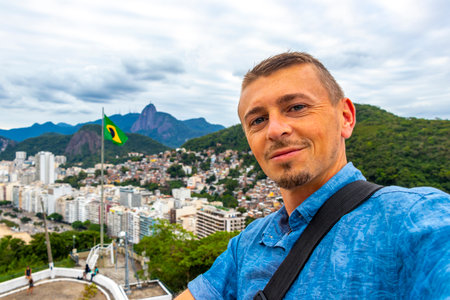 Handsome Man Tourist with the Rio de Janeiro Panorama View of the City Skyline Beaches Beach Coast Sea Mountains Tropical Forest and Blue Cloudy Sky in State of Rio de Janeiro Brazil.の写真素材