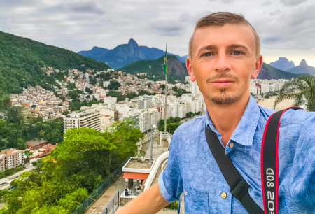 Handsome Man Tourist with the Rio de Janeiro Panorama View of the City Skyline Beaches Beach Coast Sea Mountains Tropical Forest and Blue Cloudy Sky in State of Rio de Janeiro Brazil.の写真素材