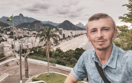 Handsome Man Tourist with the Rio de Janeiro Panorama View of the City Skyline Beaches Beach Coast Sea Mountains Tropical Forest and Blue Cloudy Sky in State of Rio de Janeiro Brazil.の写真素材