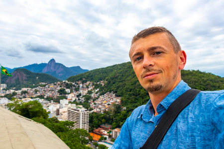 Handsome Man Tourist with the Rio de Janeiro Panorama View of the City Skyline Beaches Beach Coast Sea Mountains Tropical Forest and Blue Cloudy Sky in State of Rio de Janeiro Brazil.の写真素材