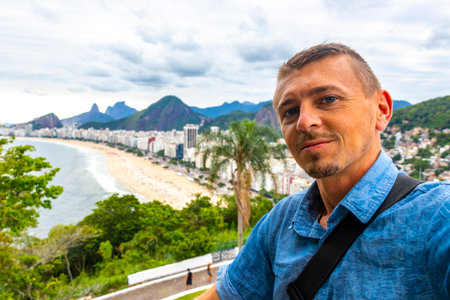 Handsome Man Tourist with the Rio de Janeiro Panorama View of the City Skyline Beaches Beach Coast Sea Mountains Tropical Forest and Blue Cloudy Sky in State of Rio de Janeiro Brazil.の写真素材
