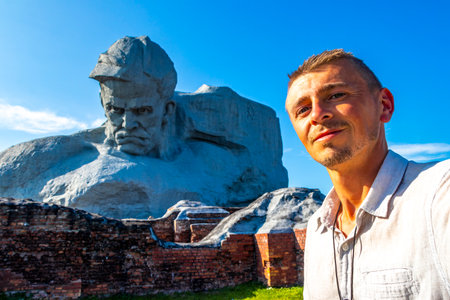 Handsome man male tourist with Monumet Muzhestvo massive gray stone rock sculpture statue at the Brest Fortress in Leninskiy Rayon Brest Brest District Brest Region Belarus.の写真素材