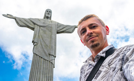 Handsome tourist traveler model and photographer at the Christ the Redeemer Cristo Redentor statue on the Corcovado mountain with blue sky panorama view in Rio de Janeiro Brazil.の写真素材