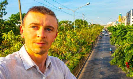 Handsome man tourist with city panorama busy street road and tropical trees in Don Mueang Bangkok...