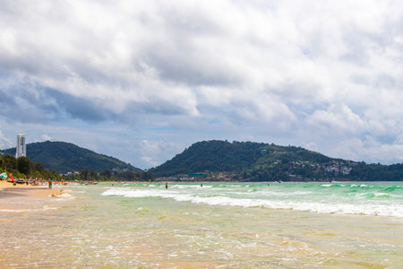 Patong Beach bay sea coast panorama view with turquoise blue clear water waves white sand and green mountains and palm trees in Patong Beach Kathu District Phuket Island Province Southern Thailand.の写真素材