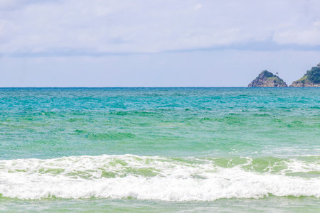 Patong Beach bay sea coast panorama view with turquoise blue clear water waves white sand and green mountains and palm trees in Patong Beach Kathu District Phuket Island Province Southern Thailand.の写真素材