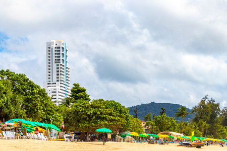 Kathu Phuket Thailand October 08, 2025 Patong Beach bay panorama view with promenade tourists people blue water waves sun loungers parasols lifeguard watch tower mountains and palm trees in Thailand.の写真素材