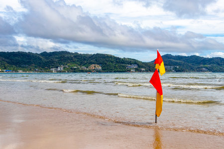 Kathu Phuket Thailand October 10, 2025 Patong Beach bay with red yellow flag warning sign here sea coast panorama view turquoise blue clear water waves mountains in Patong Phuket Island Thailand.の写真素材